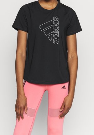 Henkilö, joka käyttää mustaa Adidasin t-paitaa valkoisella logolla ja vaaleanpunaisia Adidas-legginsejä, joissa on verkkokappaleet ja mustat raidat.