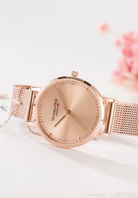 Orologio da polso Victoria Hyde London in oro rosa con cinturino in rete e quadrante minimalista con indicatori delle ore in cristallo su sfondo bianco.