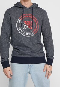 Marineblauwe gestreepte hoodie met een capuchon met trekkoorden, voorzien van een circulair logo in rood en wit. Geribde boorden bij de mouwen en zoom. Zachte stoftextuur.