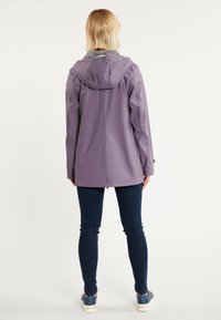 Violeta ūdensizturīga jaka ar piedurknēm ar auklu un pelēku oderi, ar elegantiem šuvumiem un brīvu piegriezumu, kombinēta ar tumšiem džinsiem.