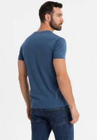Męska niebieska koszulka z krótkim rękawem wykonana z miękkiej bawełny, okrągły dekolt, prosty wzór, połączona z ciemnoniebieskimi dżinsami.