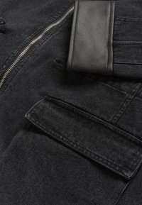 Czarna kurtka jeansowa z srebrnym suwakiem, skórzanymi akcentami i boczną kieszenią o gładkiej fakturze.