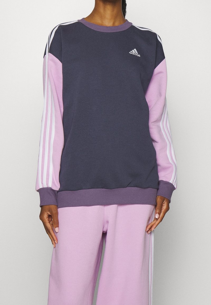Sweater met een marineblauwe romp, roze mouwen en witte drie-strepen accenten. Heeft een ronde halslijn en ribgebreide manchetten en zoom.
