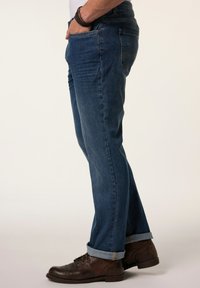 Men's dark blue denim jeans with a straight fit, cuffed hems, five-pocket design, and worn brown leather shoes.