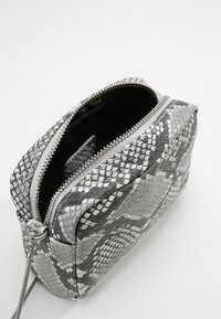 Torebka w szarym i białym wzorze imitującym wężową skórę z zamknięciem na zamek błyskawiczny, posiadająca teksturowaną powierzchnię oraz okrągły uchwyt. Kompaktowy prostokątny kształt.