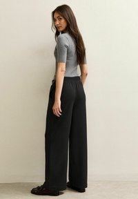 Grijze geribbelde top met korte mouwen, gecombineerd met wijde zwarte broek met elastische tailleband. Gladde textuur met een comfortabele pasvorm.