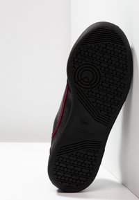 Czarne sportowe buty z teksturowaną gumową podeszwą. Posiadają czerwone i niebieskie akcenty wzdłuż boku. Gładki materiał cholewki, minimalistyczny design.