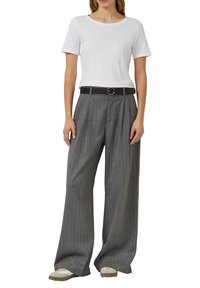 Wit T-shirt met korte mouwen gecombineerd met grijze wijde pijpen broek met krijtstreep. De broek heeft plooien aan de voorkant en een zwarte riem met een ronde gesp.