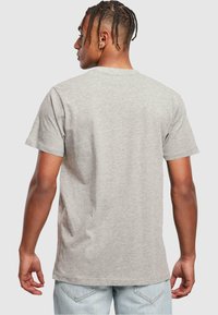 Camiseta de manga corta gris claro con cuello redondo, hecha de algodón, con una textura suave y un ajuste holgado. Vista trasera.