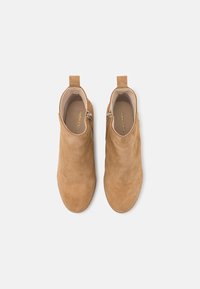 Stivaletti alla caviglia in suede tan con texture liscia, punta arrotondata, cerniere laterali e linguette per un facile indossamento. Design minimalista senza motivi.