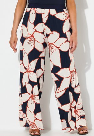 Bukser med vide ben med stort hvidt og orange blomstermønster på en mørkeblå baggrund, båret med brune åbne sandal.