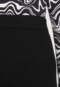 Black ribbed knit waistband transitions to a contrasting black and white abstract patterned fabric, emphasizing texture and design.