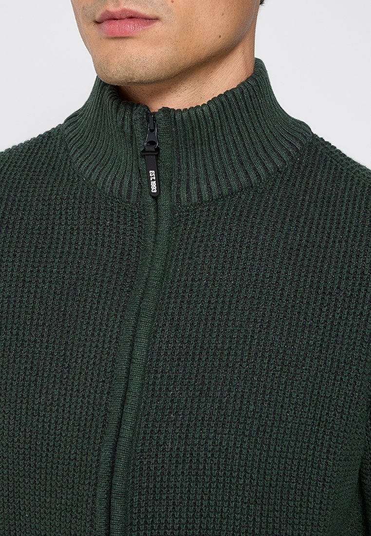 Ciemnozielony sweter dziany z wysokim prążkowanym kołnierzem i pełnym zapięciem na zamek, z teksturowanym wzorem w całej powierzchni.