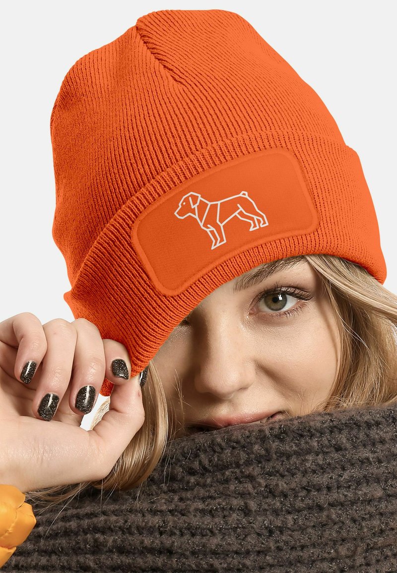 Orange knitted beanie with a textured surface and a patch featuring a white outline of a dog. The beanie is snugly fitted.