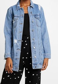 Světle modrá džínová bunda s opranými detaily, zapínáním na knoflíky a límcem. Stylizováno s černým overalem s bílými puntíky.