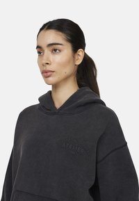 Felpa con cappuccio grigio scuro realizzata in tessuto morbido, dotata di tasca a marsupio e cappuccio con coulisse regolabile; presenta un dettaglio testuale in rilievo sul davanti.