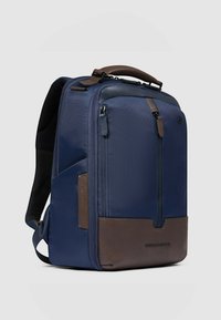 Rucksack aus marineblauem Stoff mit braunen Lederakzenten, rechteckige Form, vordere Reißverschlusstasche, gepolsterte Träger und Logodetail am unteren Rand.