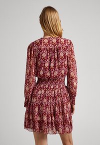 Bedrucktes Kleid mit langen, durchsichtigen Ärmeln, gesmokt in der Taille und einem plissierten Rock in den Farbtönen Burgunder, Pink und Creme mit floralen Mustern.