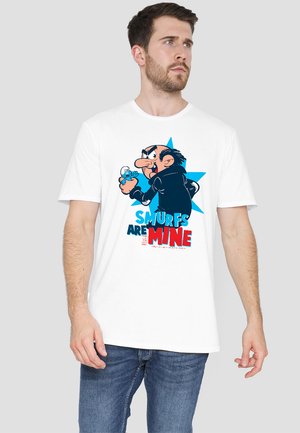 Weißes T-Shirt mit kurzen Ärmeln, das eine blaue und rosa Grafik eines Charakters zeigt, der einen Schlumpf hält, mit dickem Text: "SCHLÜMPFE GEHÖREN MIR."