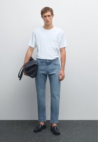 Bílá krátká tričko s kapsou, světlé modré džíny, černá kožená taška a černé mokasíny na neutrálním pozadí.