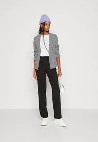 Juodas ir baltas houndstooth modelio bleiseris, baltas marškinėliai, juodos kelnės, baltos sportbačiai ir lilac spalvos kepurė. Minimalistinio stiliaus rankinė rankoje.