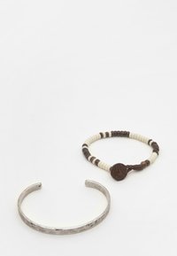 Bracciale in metallo con una finitura testurizzata affiancato a un bracciale di perline nei toni bianco, marrone e marrone scuro, con un accento circolare.