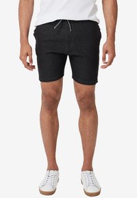 Shorts noirs en tissu doux, dotés d'une taille avec cordon de serrage et d'une coupe ajustée. Portés avec des baskets blanches pour un look décontracté.