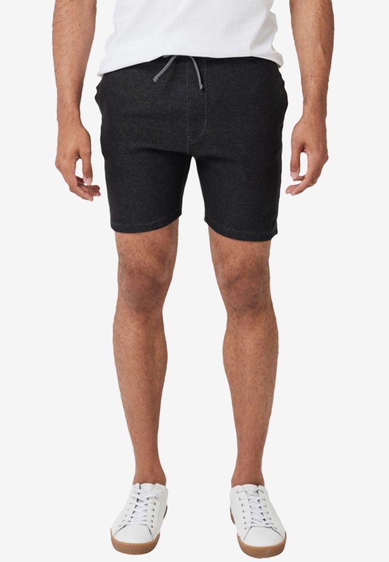 Shorts noirs en tissu doux, dotés d'une taille avec cordon de serrage et d'une coupe ajustée. Portés avec des baskets blanches pour un look décontracté.
