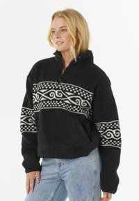 Pullover in pile nero con collo a zip, caratterizzato da un motivo tribale bianco sul petto e tasche sul davanti. Texture morbida.