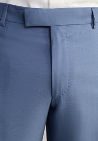 Pantalons bleu clair en tissu texturé, présentant une coupe droite, un devant plat et des poches latérales avec une taille lisse.