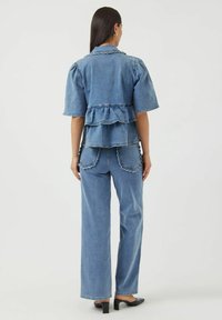 Denim-asuste, joka sisältää frillattuja, kerroksellisia peplum-toppeja, leveälahkeisia housuja, joissa on kaarevat taskureunat, ja keskipitkä sininen pesu.