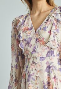 Vestido floral de tejido ligero con una base crema. Presenta mangas con volantes, un escote en V y botones rosas en el frente.