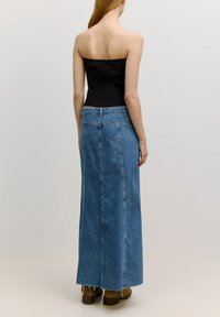 Lange denim rok in lichtblauw met een hoge taille en contrasterende stiksels. Heeft een ruwe rand en discrete achterzakken. Gepaard met bruine enkellaarsjes.