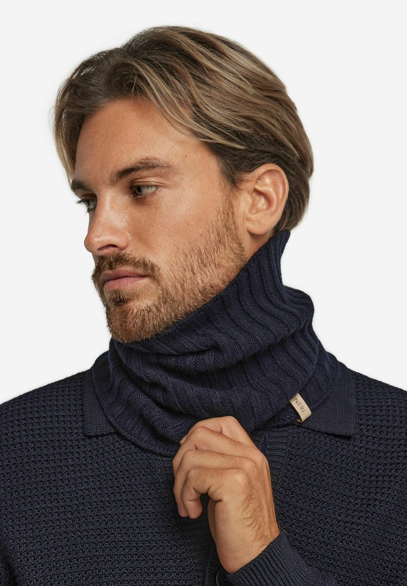 Navyblauwe geribbelde coltrui met een gestructureerd patroon, voorzien van een omgeslagen kraag en een klein merklabel aan de zijkant.