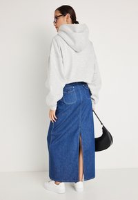 Hoodie cinza com capuz, emparelhado com uma saia maxi de ganga com uma fenda nas costas e dois bolsos traseiros. Ténis brancos e bolsa preta.