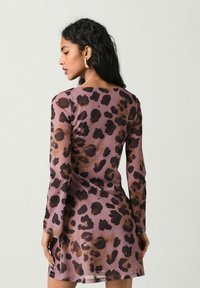 Dlouhé šaty s dlouhým rukávem z průhledné mauve látky, která má výrazný leopardí vzor v tmavě hnědé barvě, s přiléhavým střihem a rovnými lemy.