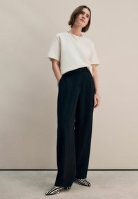 White short-sleeve top paired with high-waisted black wide-leg trousers and black and white striped slip-on shoes. Simple chain necklace.