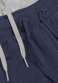 Marineblauwe sweatpants met een grijze tailleband, uitgerust met twee trekkoorden—één grijs, één marineblauw—door oogjes, met een zachte textuur.