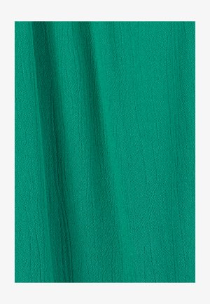 Tissu vert avec un tissage finement texturé et des plis verticaux doux créant des ombres subtiles.