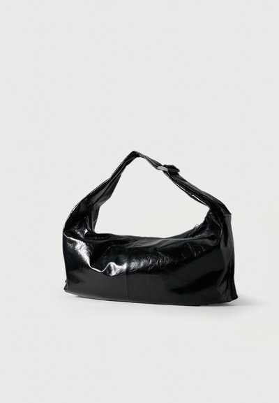 Sac à épaule en cuir noir brillant de forme en croissant avec une bandoulière unique sur un fond clair uni.