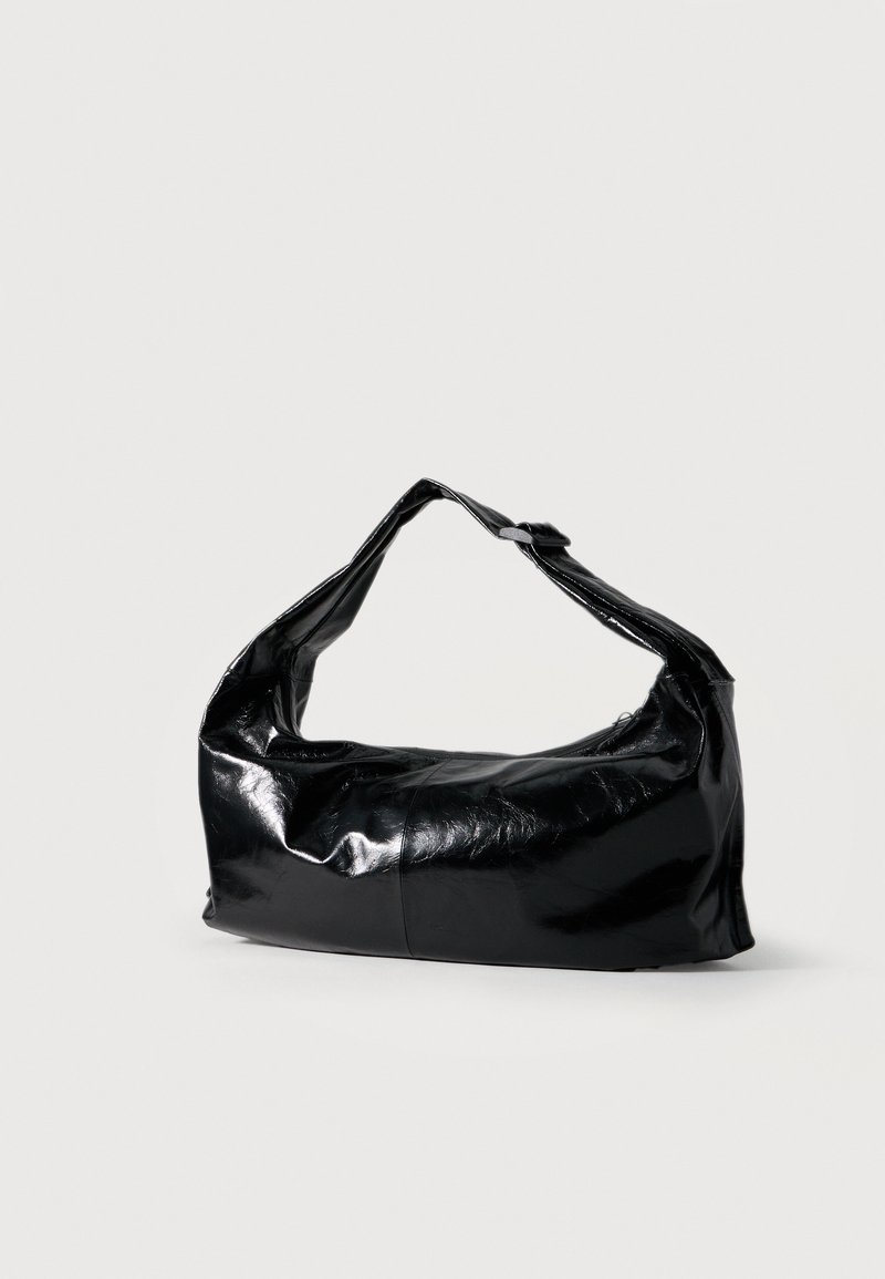 Sac à épaule en cuir noir brillant de forme en croissant avec une bandoulière unique sur un fond clair uni.