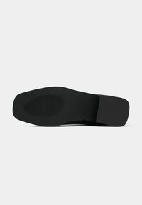 Semelle extérieure de chaussure noire présentant une finition lisse et un motif de grip texturé. Bout carré et talon bloc avec un design minimaliste.