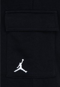 Crni materijal s teksturiranim džepom i bijelim Jumpman logom izvezenim na dnu. Jednostavan, funkcionalan dizajn.