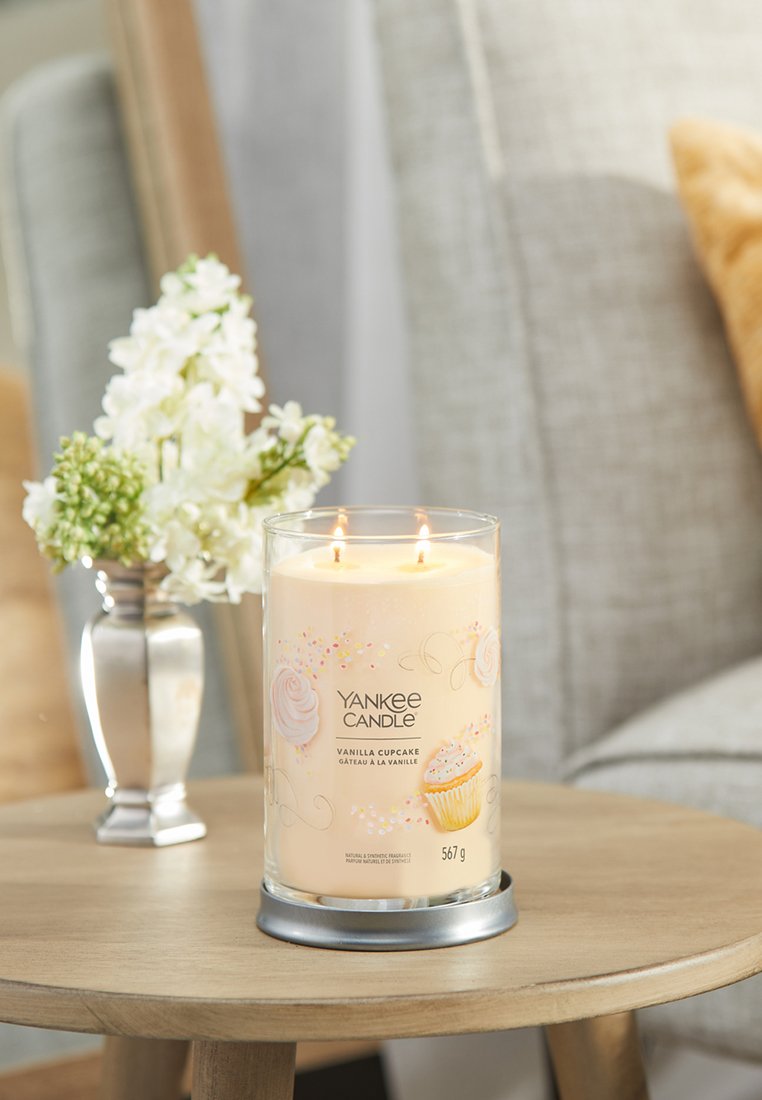 Yankee Candle in einem klaren Glasbehälter, gefüllt mit hellbeigem Wachs, beschriftet mit "Vanilla Cupcake", mit zwei Dochten und dekorativen pastellfarbenen Akzenten.