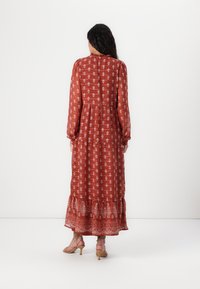 Robe longue couleur rouille avec des motifs floraux blancs, taille froncée et ourlet évasé. Elle a des manches longues et un col haut.