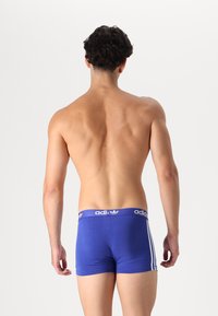Kék pamut boxeralsó fehér Adidas logós derékrésszel és három fehér csíkkal az oldalán, amely szoros illeszkedést és sima textúrát mutat.