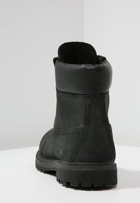 Bottine en cuir noir avec semelle robuste, design sans couture et dessus arrondi doux. Présente des coutures contrastantes et un détail logo.