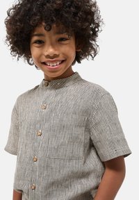 Chemise à manches courtes rayée beige et noire, dotée d'un col montant, de boutons en bois et d'une poche poitrine. Fabriquée en tissu texturé.