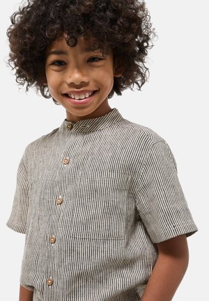 Chemise à manches courtes rayée beige et noire, dotée d'un col montant, de boutons en bois et d'une poche poitrine. Fabriquée en tissu texturé.