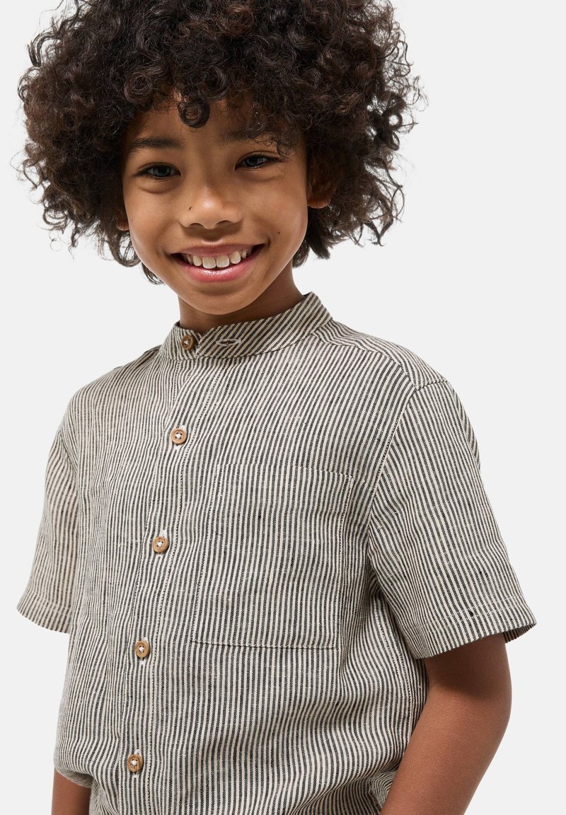 Chemise à manches courtes rayée beige et noire, dotée d'un col montant, de boutons en bois et d'une poche poitrine. Fabriquée en tissu texturé.